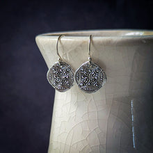 Load image into Gallery viewer, Silver earrings with intricate designs hanging from a ceramic vase against a dark background