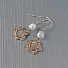 Load image into Gallery viewer, A pair of handmade dangle earrings featuring oxidized bronze flower charms, textured white pearl beads, and silver fishhook wires, displayed on a gray wood-grain surface.