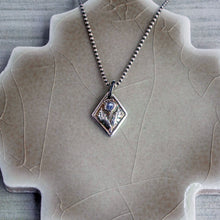 Load image into Gallery viewer, A fine silver thistle with a blue tanzanite on a chain against a textured background