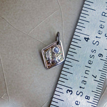Load image into Gallery viewer, A fine silver thistle pendant with a blue tanzanite centerpiece, attached to a silver chain, displayed next to a ruler for scale