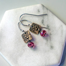 Load image into Gallery viewer, A pair of handmade dangle earrings with textured bronze square charms, silver fishhook wires, and faceted pink tourmaline beads, displayed on a white hexagonal stone tray.