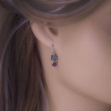 Load image into Gallery viewer, A close-up of a small dangle earring worn on a model's ear. The earring features a square bronze charm and a small dangling dark pink gemstone.