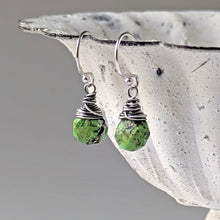 Load image into Gallery viewer, Green stone earrings with silver wire wrapping dangle from a decorative bowl