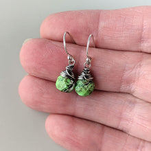 Load image into Gallery viewer, Green stone earrings with silver wire wrapping held between fingers on a neutral background