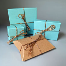 Load image into Gallery viewer, Turquoise gift boxes and a brown pillow-shaped box with gold ribbons on a gray background