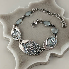 Load image into Gallery viewer, Silver bracelet with intricate designs and gemstones on a textured surface