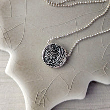 Load image into Gallery viewer, Reverse side of necklace with a detailed silver pendant on a textured surface.