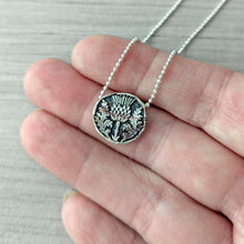 Load image into Gallery viewer, Silver necklace with a detailed thistle
pendant held between fingers on a light gray background