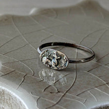 Load image into Gallery viewer, Silver ring with a detailed design on a textured ceramic surface