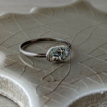 Load image into Gallery viewer, Silver ring with a detailed design on a textured ceramic surface
