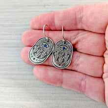 Load image into Gallery viewer, Silver earrings with blue stones held between fingers for scale on a light gray background