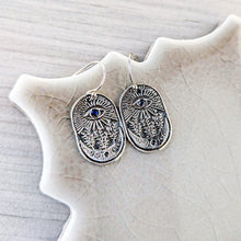 Load image into Gallery viewer, Silver earrings with an eye design on a textured surface.