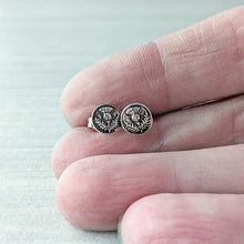 Load image into Gallery viewer, Small silver earrings held between fingers on a light background