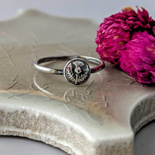 Load image into Gallery viewer, Silver ring with a floral design on a textured surface with a pink flower.