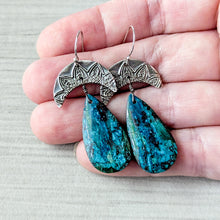 Load image into Gallery viewer, Pair of earrings with blue teardrop-shaped stones held between fingers on a light background