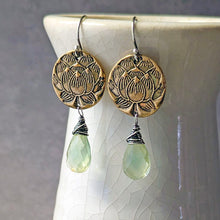 Load image into Gallery viewer, A pair of bohemian-style dangle earrings with antique bronze lotus medallions and light green faceted gemstone drops, displayed on a white ceramic vase against a gray background.