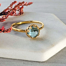 Load image into Gallery viewer, Gold ring with a clear blue green gemstone on a white surface with red flowers.