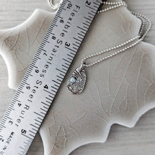 Load image into Gallery viewer, Silver necklace with a pendant on a ceramic tile next to a ruler for scale.