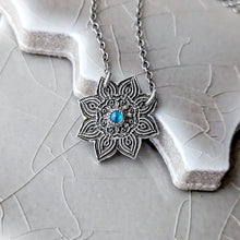 Load image into Gallery viewer, Silver mandala pendant with a blue gemstone on a textured stone surface
