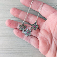 Load image into Gallery viewer, Silver floral necklace with pink stones held in a hand against a neutral background