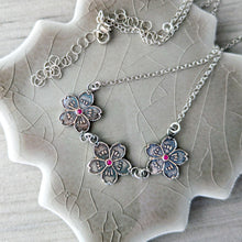 Load image into Gallery viewer, Silver necklace with floral pendants with rubies on a textured ceramic surface