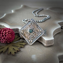 Load image into Gallery viewer, Decorative silver pendant with green gemstone on a textured surface with a pink flower and leaf.