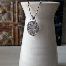 Load image into Gallery viewer, A silver necklace with an intricately designed pendant depicting a flying bat with a pale gray stone hanging from a white vase with a blurred background