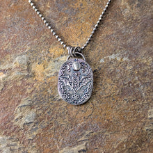 Load image into Gallery viewer, A silver necklace with an intricately designed pendant depicting a flying bat with a pale gray stone laying on a stone tile