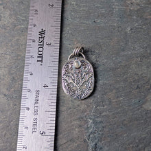 Load image into Gallery viewer, A silver necklace with an intricately designed pendant depicting a flying bat with a pale gray stone laying on a slate tile with a ruler for scale