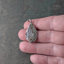 Load image into Gallery viewer, A teardrop shaped silver pendant with a green faceted stone held in a hand for size context