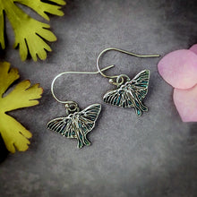 Load image into Gallery viewer, Silver Luna moth earrings on a gray surface with leaves and flowers.