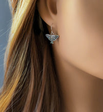 Load image into Gallery viewer, Close-up of a person wearing a silver Luna moth earring with a blurred background