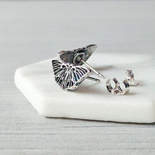 Load image into Gallery viewer, Butterfly-shaped silver earrings on a white stone surface