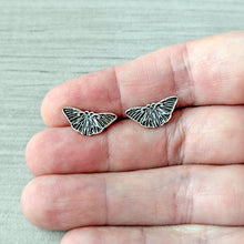 Load image into Gallery viewer, Butterfly-shaped earrings held between fingers on a light gray background