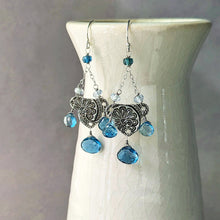Load image into Gallery viewer, Silver earrings with blue gemstones on a white stand against a gray background