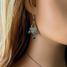 Load image into Gallery viewer, Close-up of a person wearing silver earrings with blue gemstones.