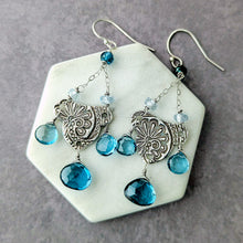 Load image into Gallery viewer, Pair of earrings with London blue topaz beads and silver filigree on a hexagonal stone surface.