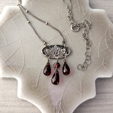 Load image into Gallery viewer, Silver necklace with irises pendant and red gemstones on a textured surface