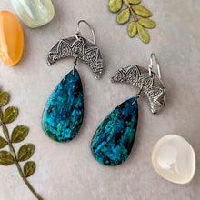 Load image into Gallery viewer, Blue teardrop earrings with silver crescent moon pendants on a textured surface with leaves and stones.