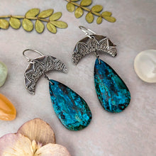 Load image into Gallery viewer, Pair of silver earrings with blue teardrop stones on a textured surface with leaves and flowers.