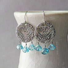 Load image into Gallery viewer, Silver earrings with an embossed owl design and blue teardrop gemstone beads on a white ceramic stand.