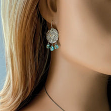 Load image into Gallery viewer, Close-up of a woman wearing silver earrings with an embossed owl design and blue teardrop gemstone beads.
