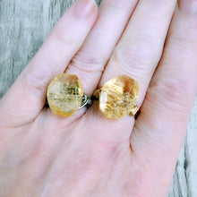 Load image into Gallery viewer, 2 rings with a large, faceted yellow gemstones one on silver wire, the other on gold wire, worn on a hand for scale