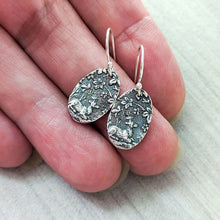 Load image into Gallery viewer, Silver earrings with intricate designs held between fingers for scale on a light background