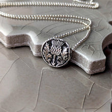 Load image into Gallery viewer, Silver necklace with a detailed floral pendant on a textured surface