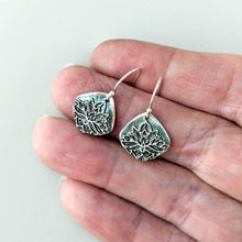 Load image into Gallery viewer, Silver floral earrings held between fingers on a light background