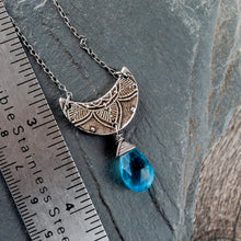 Load image into Gallery viewer, Silver crescent moon necklace with a blue pendant on a gray stone surface next to a ruler.
