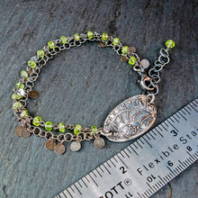 Load image into Gallery viewer, Bracelet with green beads and leaf charm on a dark stone surface with a ruler for scale.
