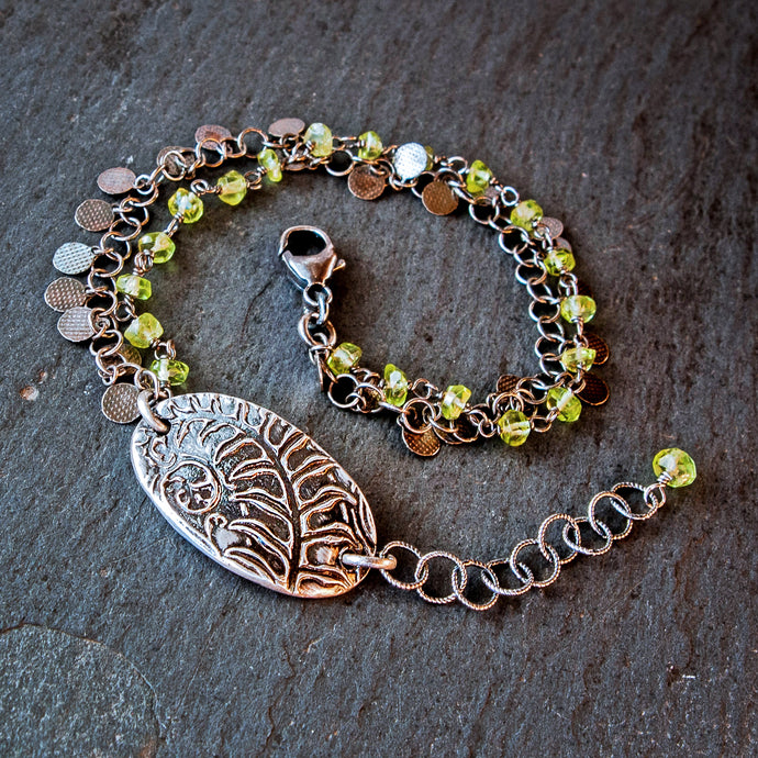 Bracelet with botanical charm and green beads on a dark surface