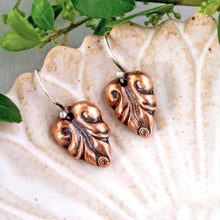Load image into Gallery viewer, A pair of copper leaf-shaped drop earrings with silver hooks, displayed on a textured ceramic leaf-shaped plate with green leaves in the background.
